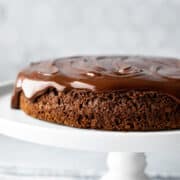 side view of vegan ganache topped chocolate cake on a white cake stand.