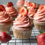vegan strawberry cupcakes on a cooling rack with strawberries nearby.