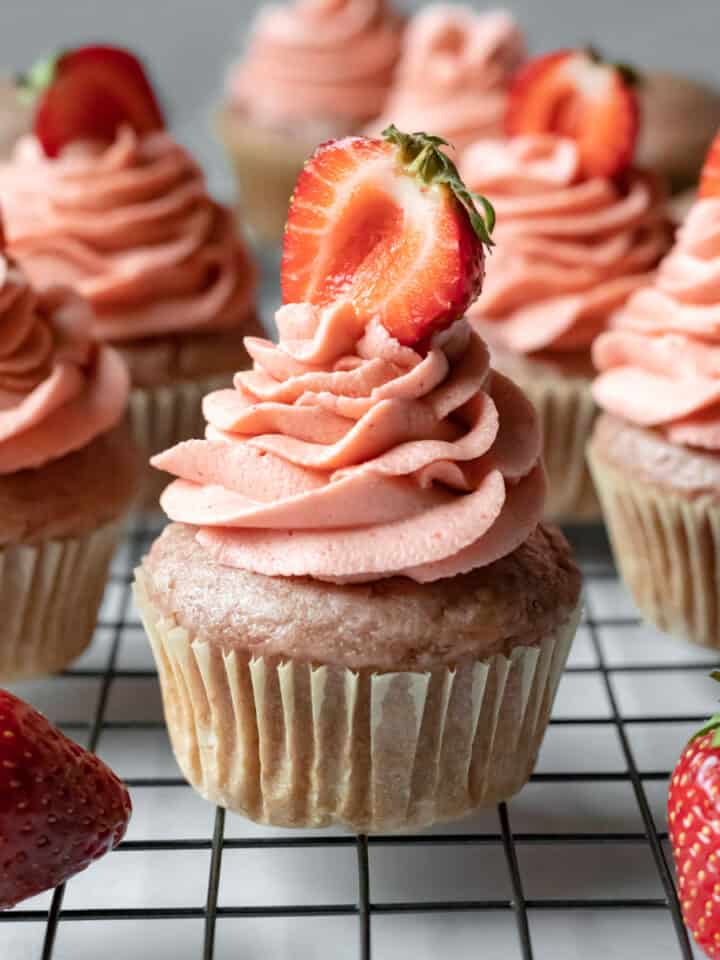 vegan strawberry cupcakes on a cooling rack with strawberries nearby.
