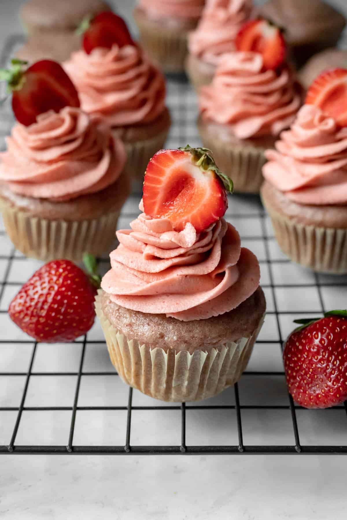 frosted strawberry cupcakes lined up on a cooling rack.
