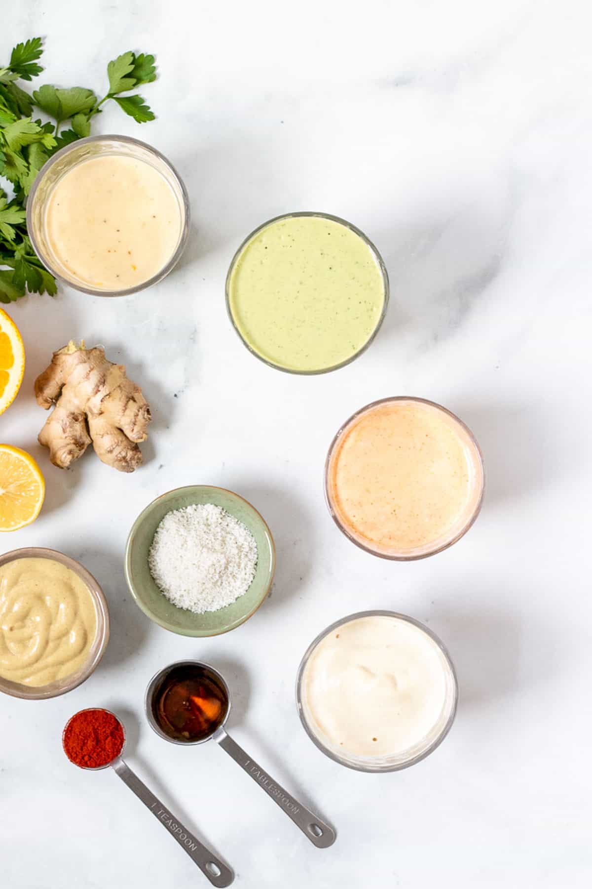 four flavorful versions of tahini salad dressing with other ingredients nearby.