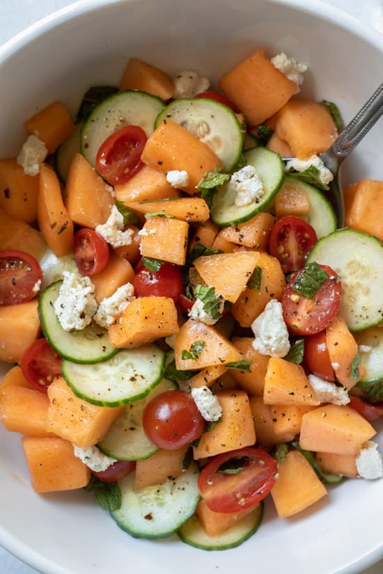 close up of a bowl full of cantaloupe salad with cucumber and mint.