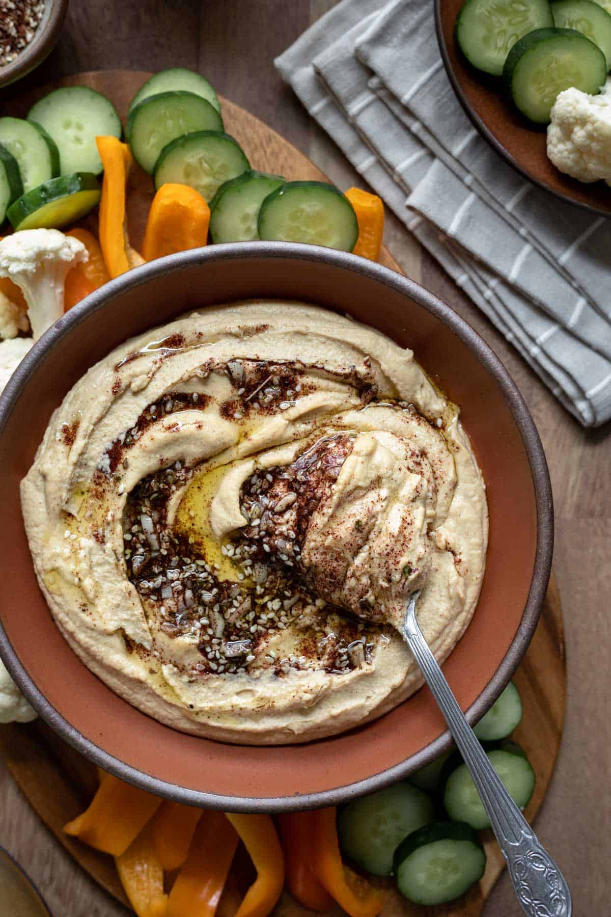 creamy hummus topped with a swirl of za'atar and garlic infused oil on a platter surrounded by raw vegetables.