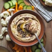 overhead view of a bowl full of zaatar hummus surrounded by raw veggies on a serving board.