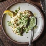 a single cauliflower steak on a plate drizzled with parsley sauce.