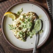a single cauliflower steak on a plate drizzled with parsley sauce.