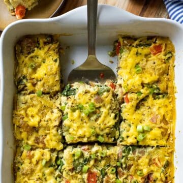 colorful breakfast casserole cut into square servings with a spatula removing a piece.