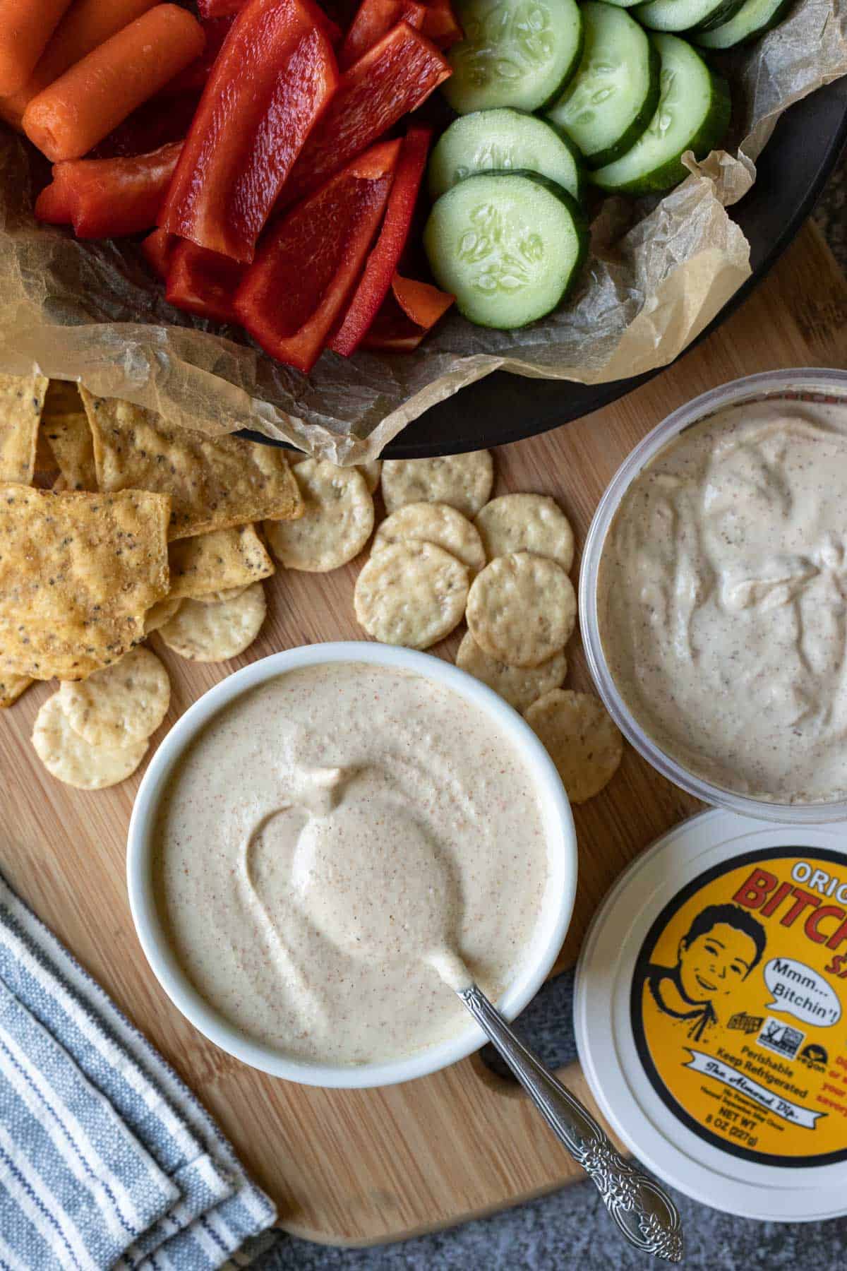 bowl of cheesy almond sauce on a wood board next to a container of Bitchin' Sauce original.