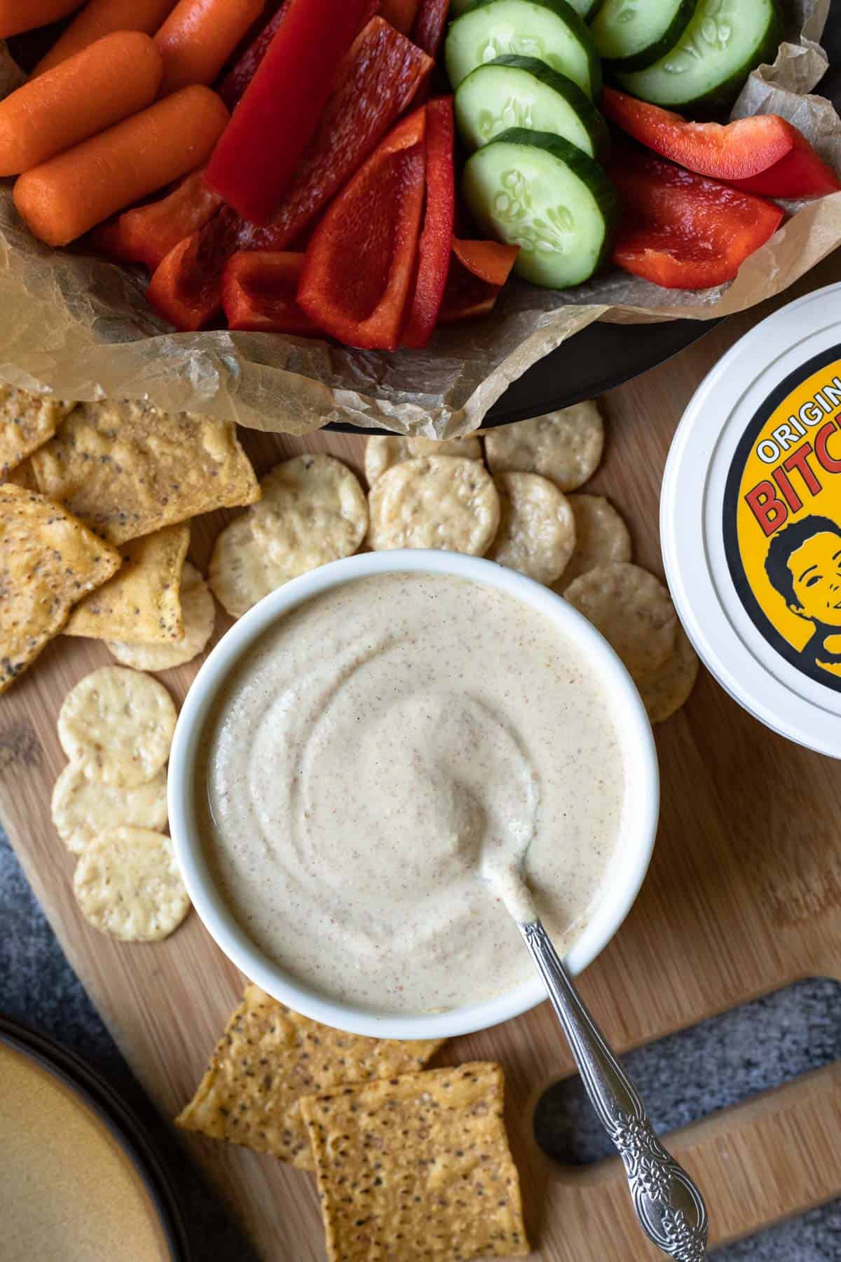 a spoon resting in homemade almond bitchin sauce surrounded by chips and crackers.