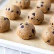 plain cookie dough bites lined up on a parchment-lined baking pan.