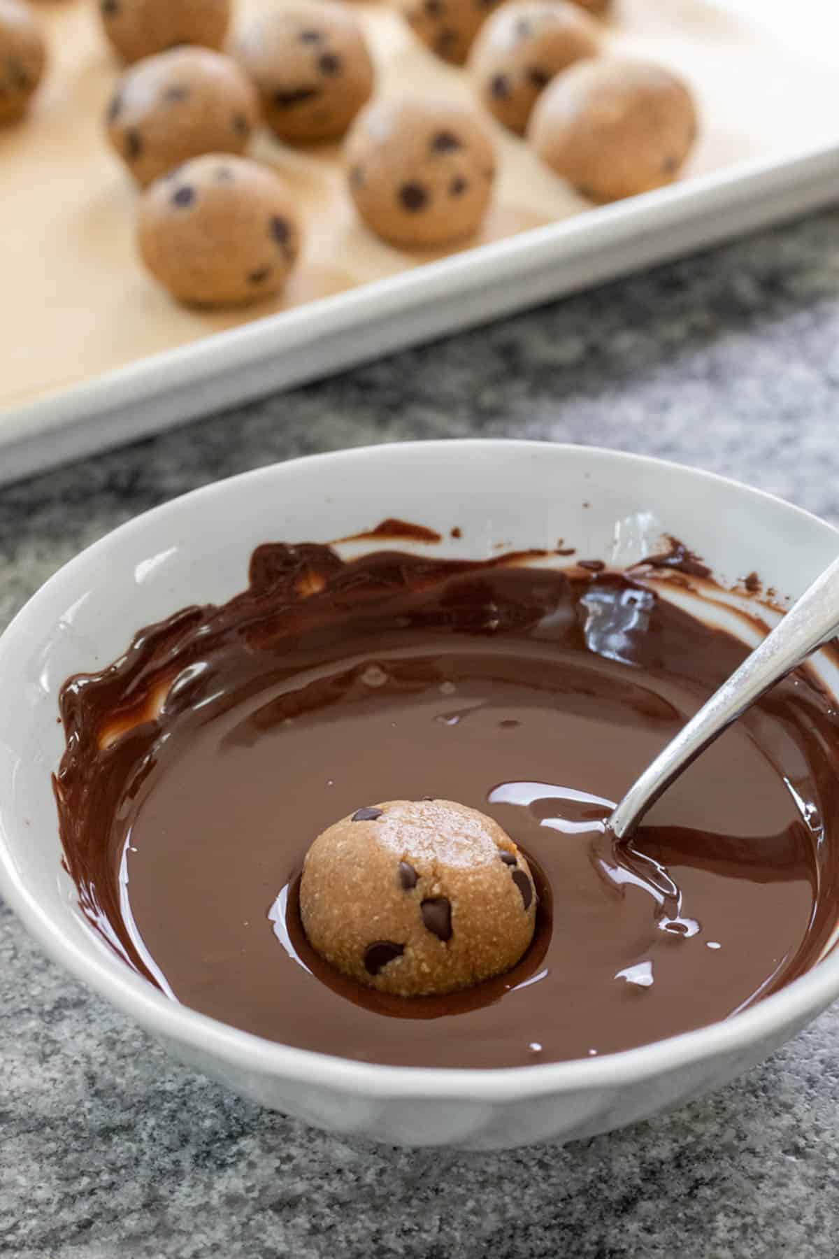 a cookie dough bite resting in a bowl full of melted chocolate.