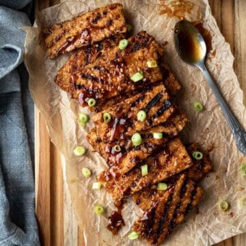 Sticky Korean BBQ tempeh laid out on a parchment-paper lined wood cutting board.