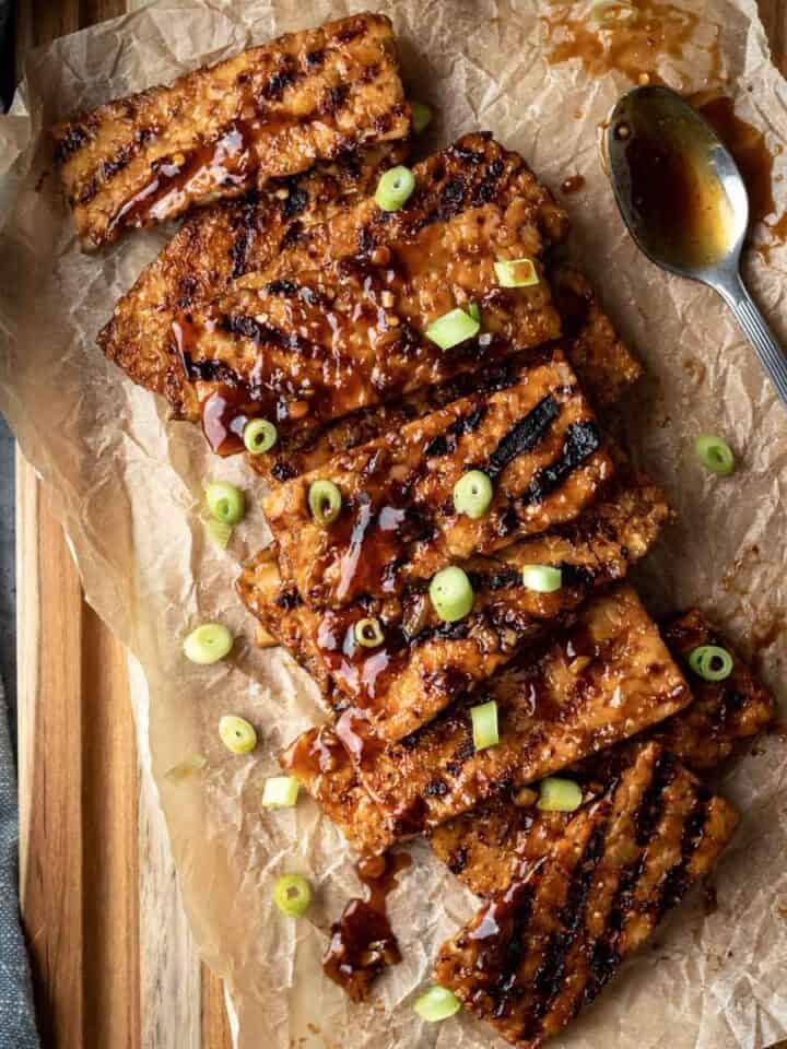Sticky Korean BBQ tempeh laid out on a parchment-paper lined wood cutting board.