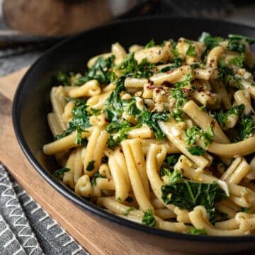 vegan garlic butter casarecce pasta with kale and lemon zest in a black bowl.
