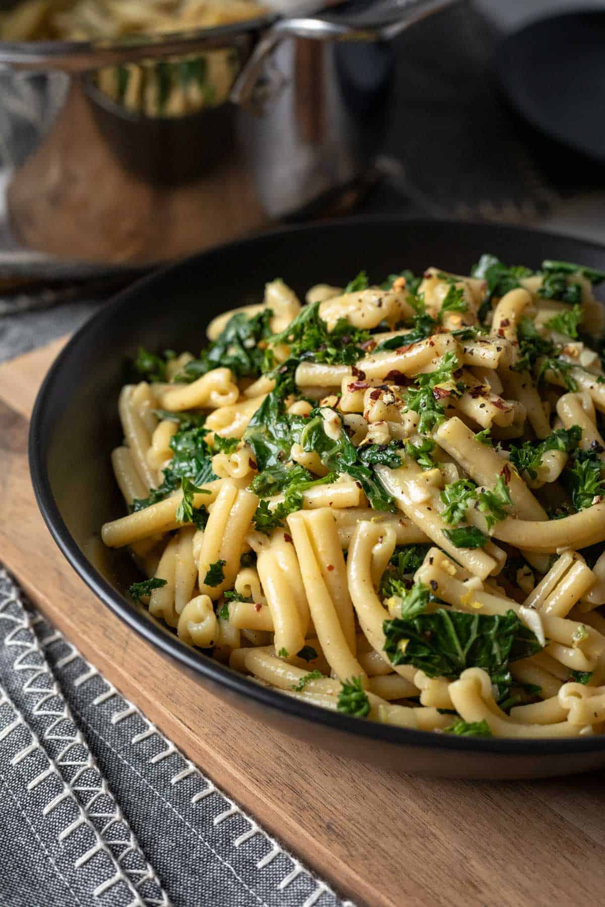 black serving bowl filled with garlic butter pasta with a pot in background.