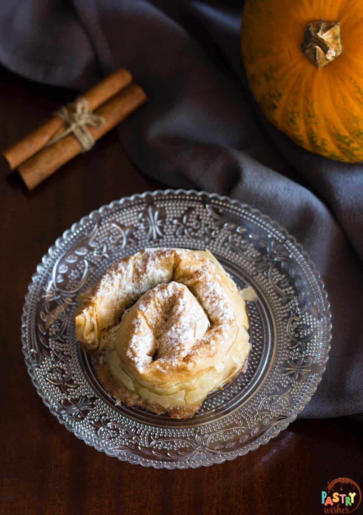 a dimly lit tablescape with a spiral phyllo hand pie on a plate and a pumpkin in the background.