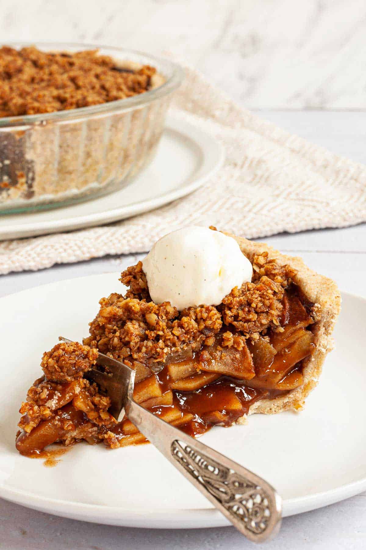 a slice of vegan apple pie with a crisp crumb sprinkle and scoop of vanilla ice cream on top.