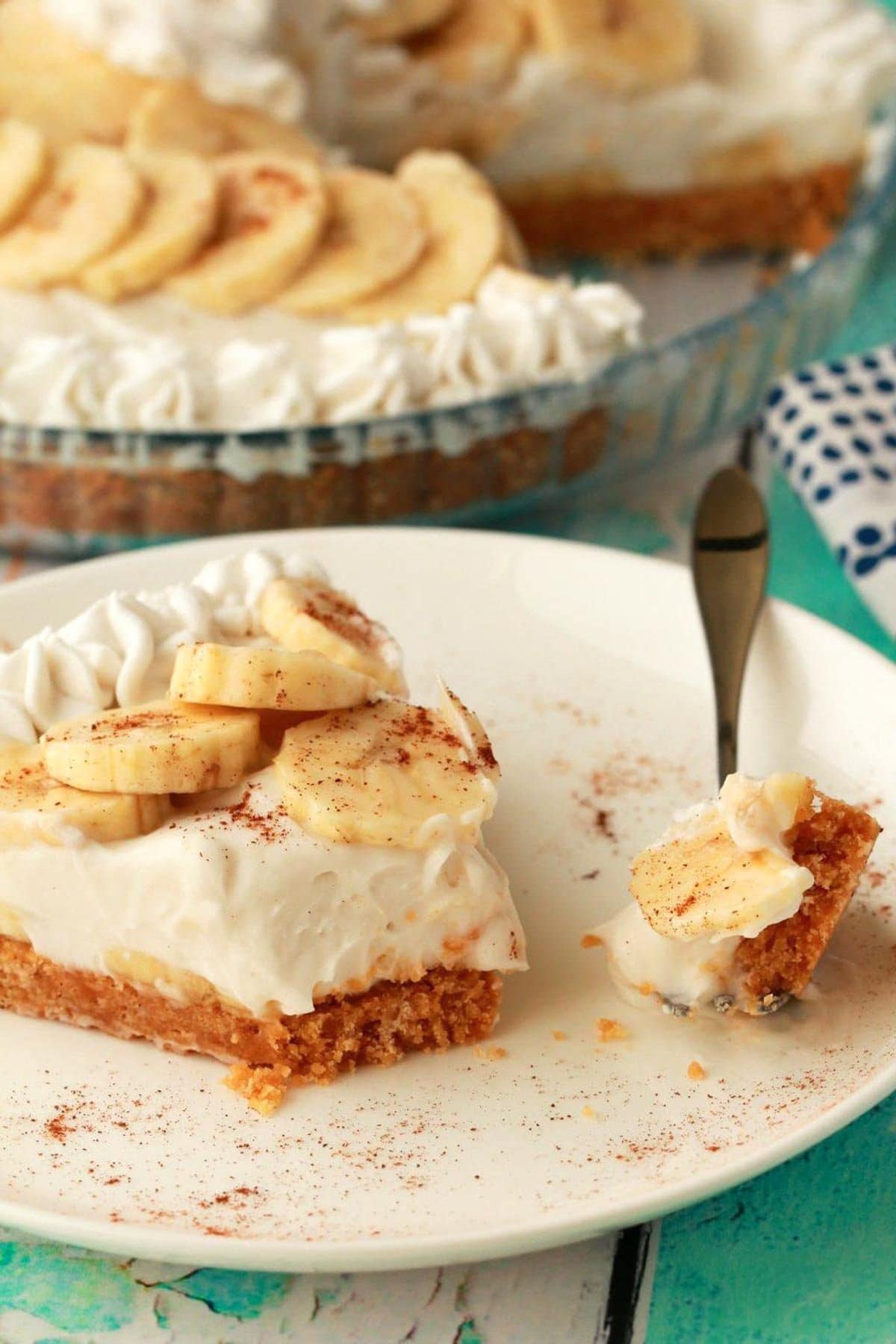 bite of vegan banana cream pie on a fork next to a slice with whole pie in background.
