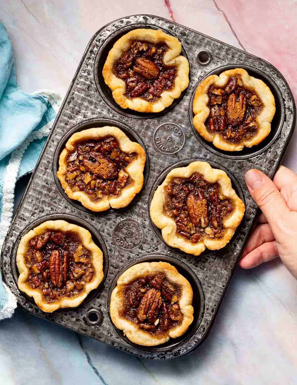 six mini tarts in an antique tin held by a hand.