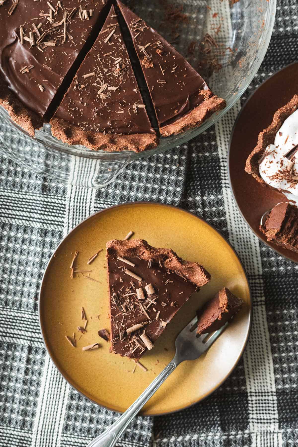 a slice of vegan chocolate pie on a yellow plate with the whole pie nearby.