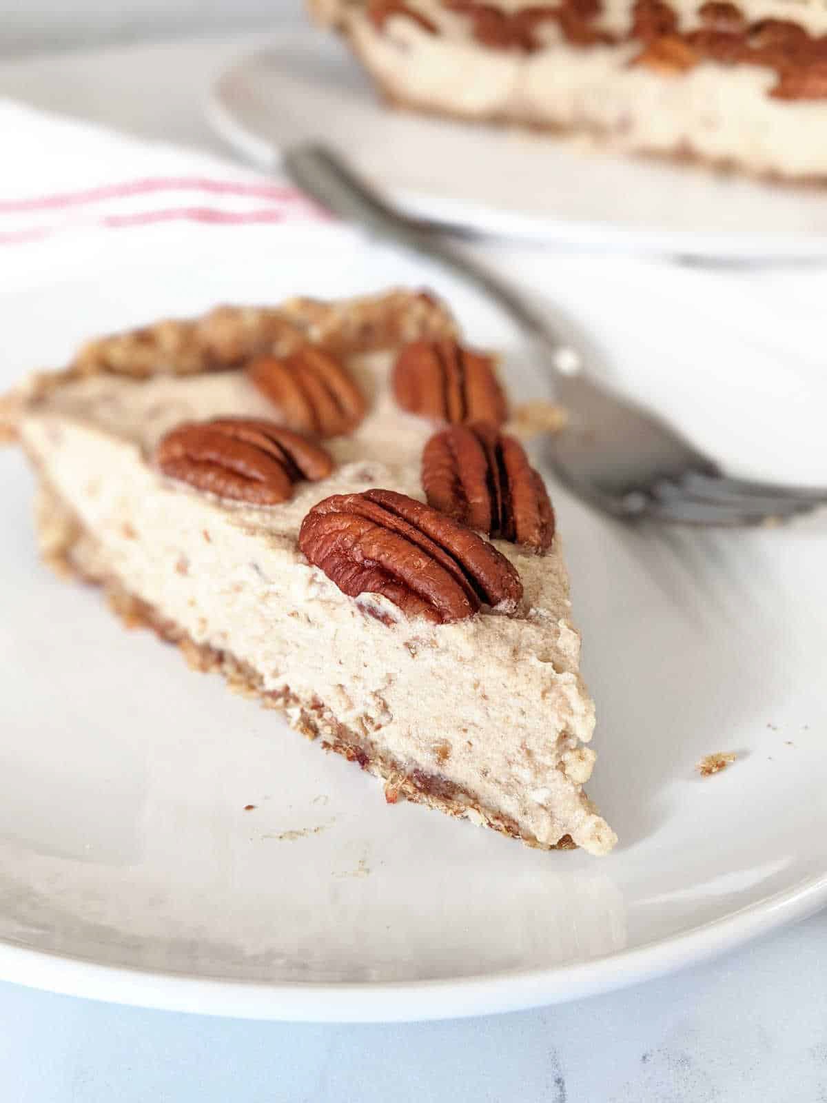 a slice of creamy pie with oat date crust and pecans on top.