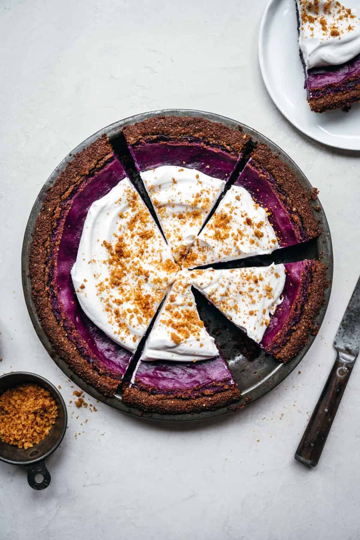 purple sweet potato pie topped with whipped cream in a metal pie tin.