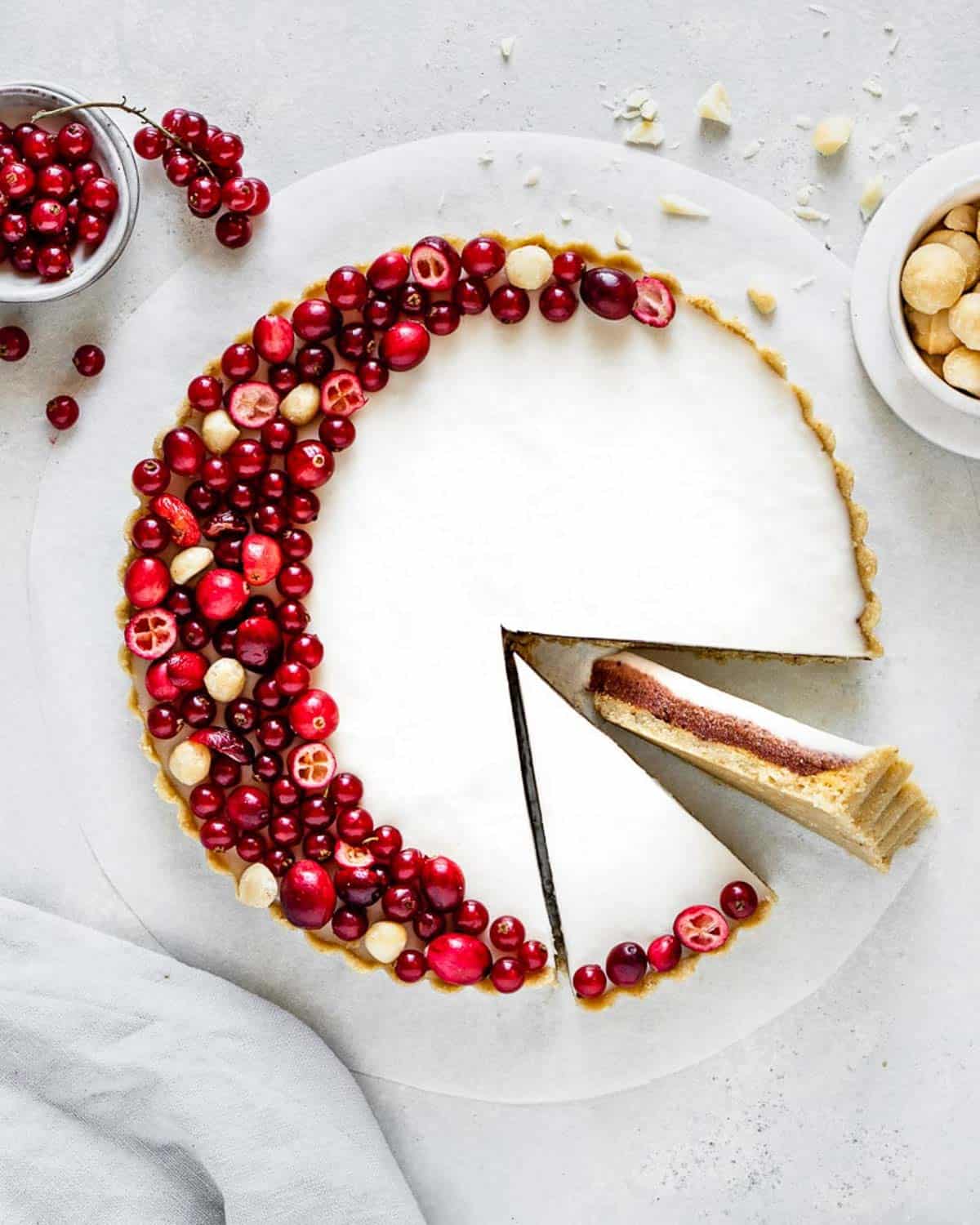 a crisp white tart decorated with cranberries with a slice turned on its side to show the layers within.