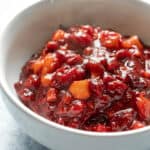 close up of cranberry apple compote in a white bowl showing the chunky fruit texture and vibrant color.
