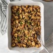 White baking dish with shiitake mushroom stuffing and a serving spoon resting on the side.