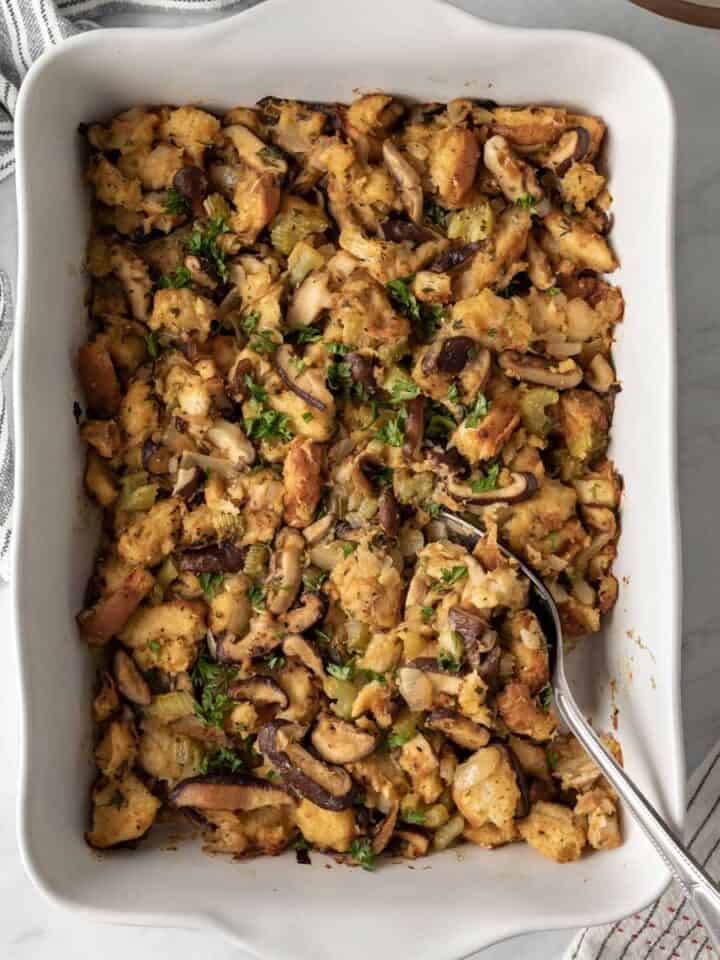 White baking dish with shiitake mushroom stuffing and a serving spoon resting on the side.