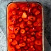 vibrant red homemade strawberry jel on top of pretzel dessert with sliced strawberries suspended inside.