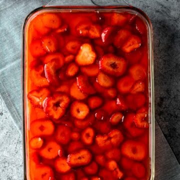 vibrant red homemade strawberry jel on top of pretzel dessert with sliced strawberries suspended inside.