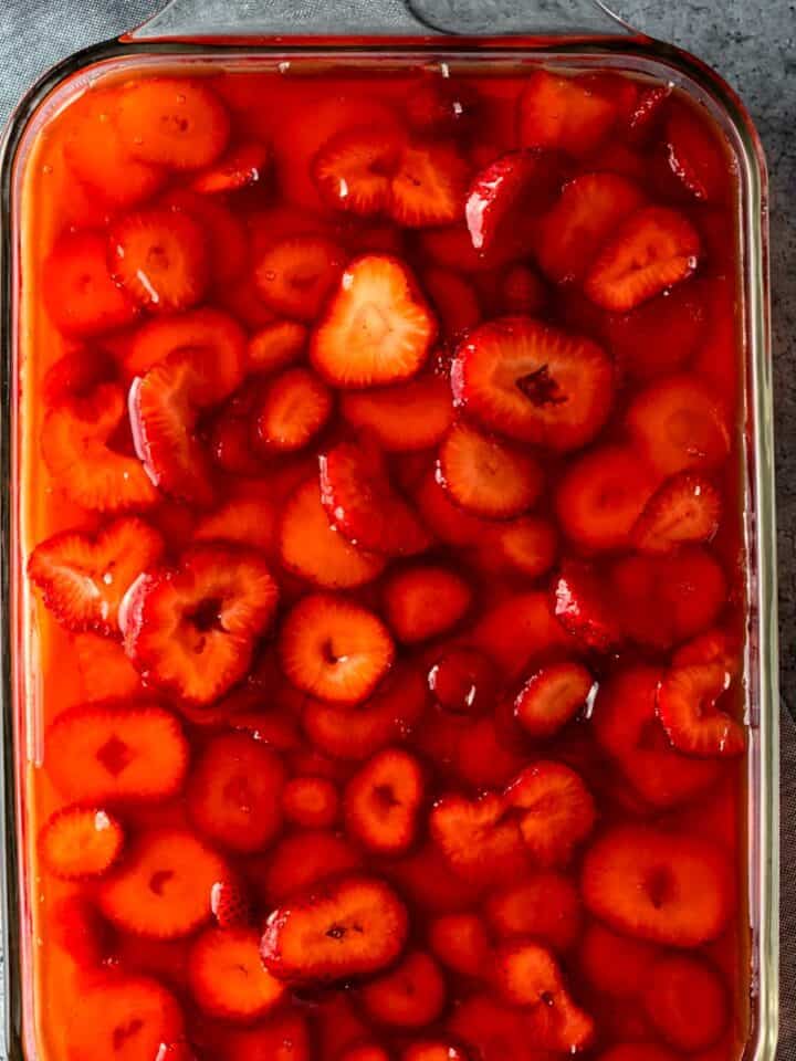 vibrant red homemade strawberry jel on top of pretzel dessert with sliced strawberries suspended inside.