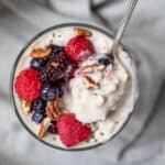 vegan protein oatmeal with berries and nuts in a glass jar with a spoon scooping up a bite.