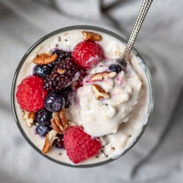 vegan protein oatmeal with berries and nuts in a glass jar with a spoon scooping up a bite.