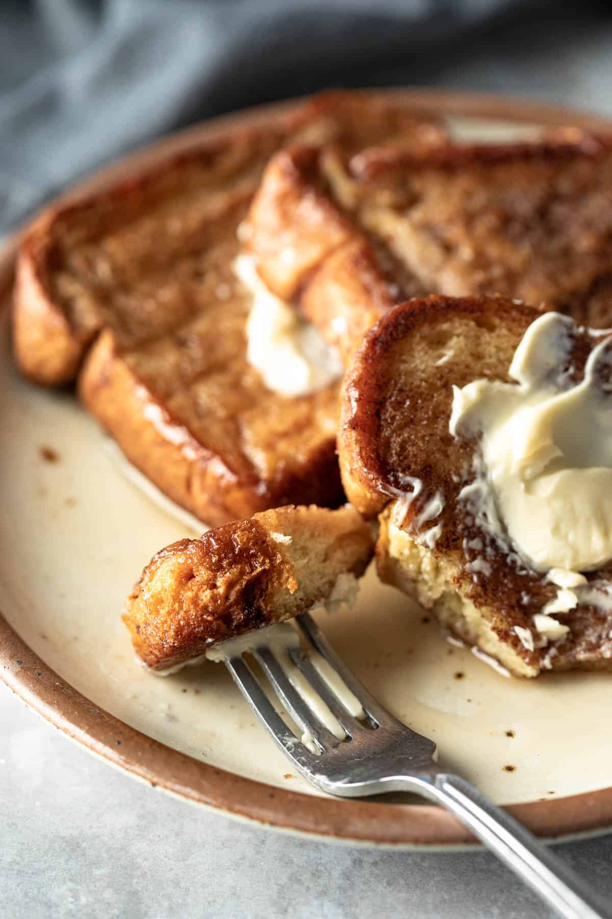 close up of a bite of French toast on a fork resting on a plate.
