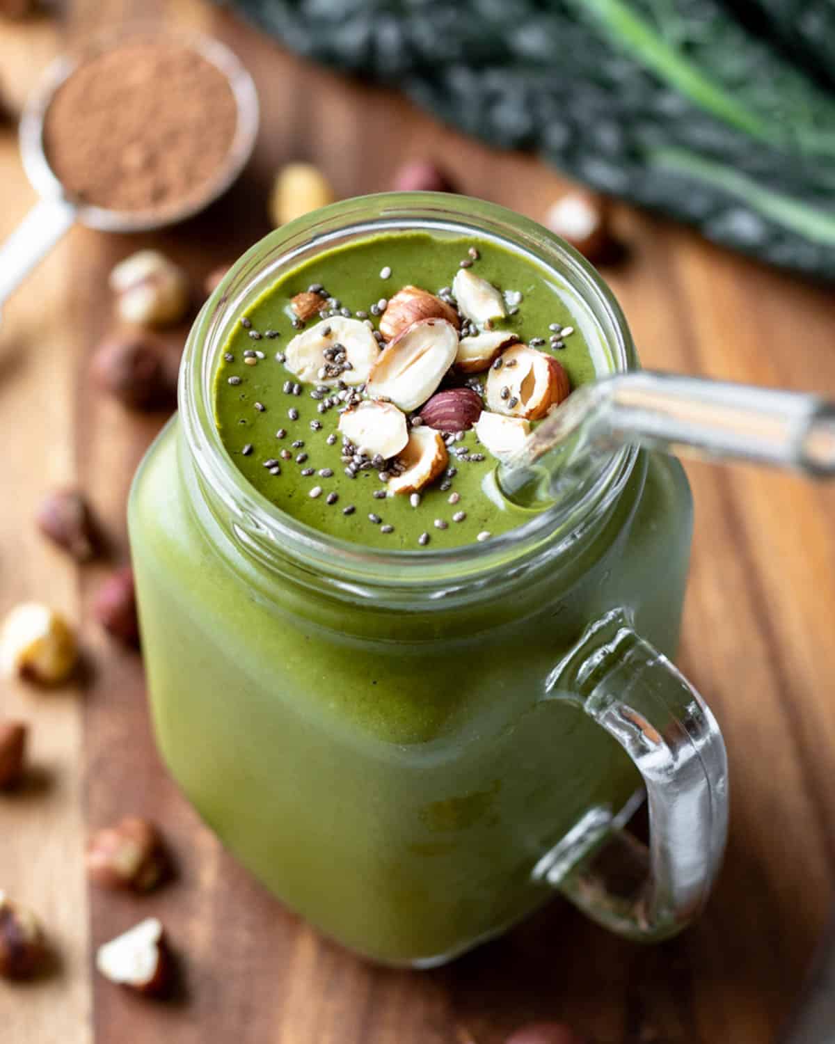 kale smoothie in a glass mug with hazelnuts and chia seeds sprinkled on top.