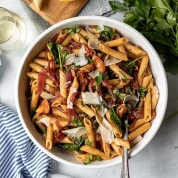 large bowl full of vegan pasta with onion, spinach, vegan cheese, and fresh parsley.