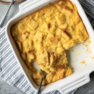 a serving spoon scooping up golden yellow pineapple stuffing from a white square baking dish.