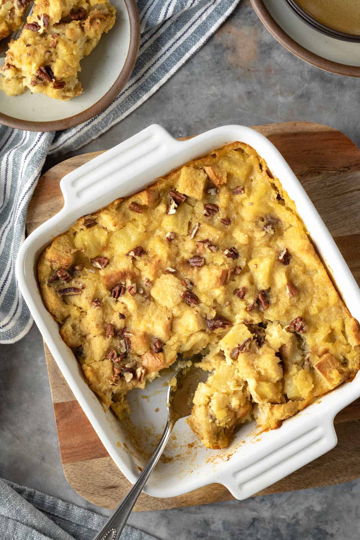 white baking dish full of pineapple casserole and a serving spoon resting on the side.