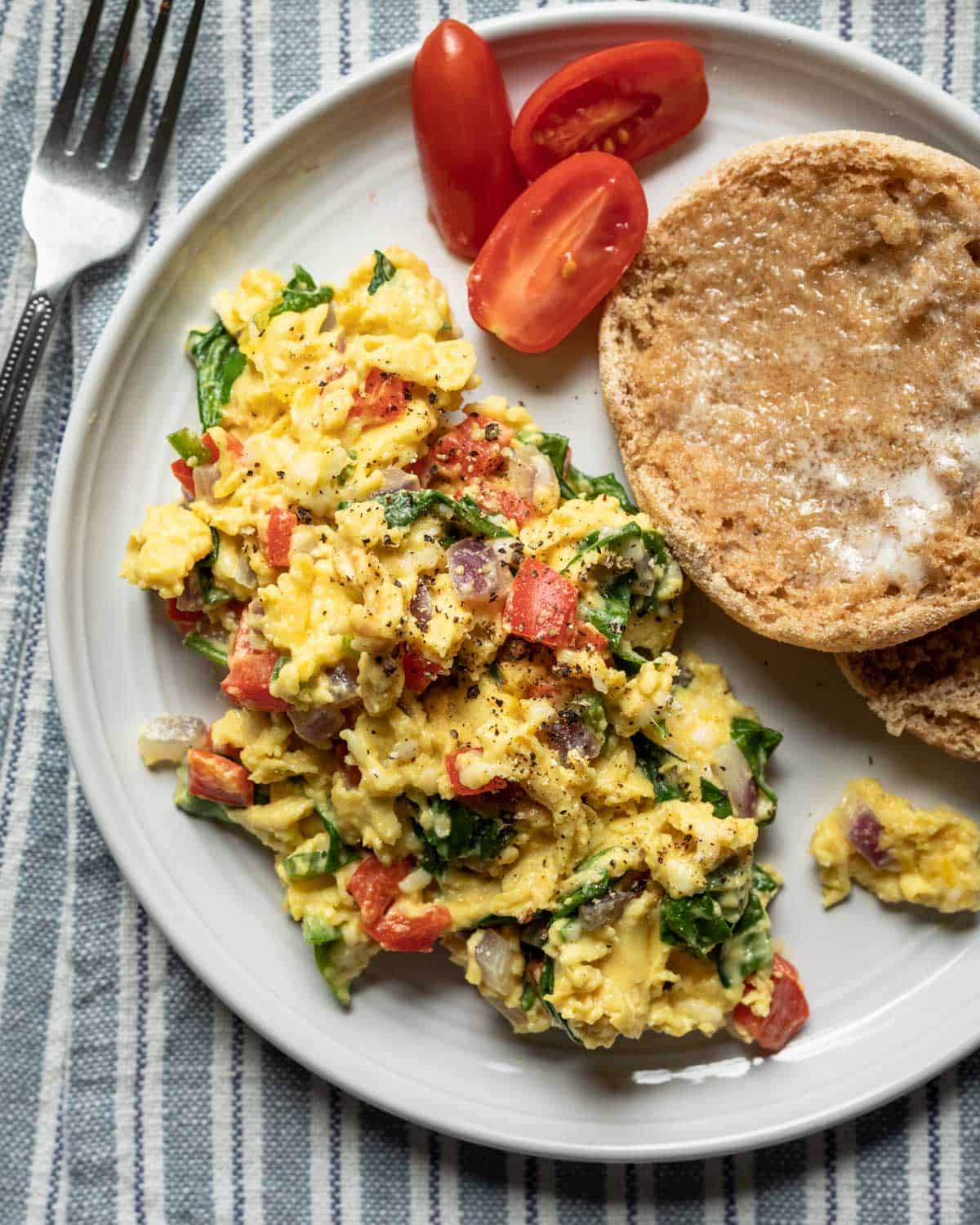 scrambled JUST Egg with vegetables on a plate with an English muffin.