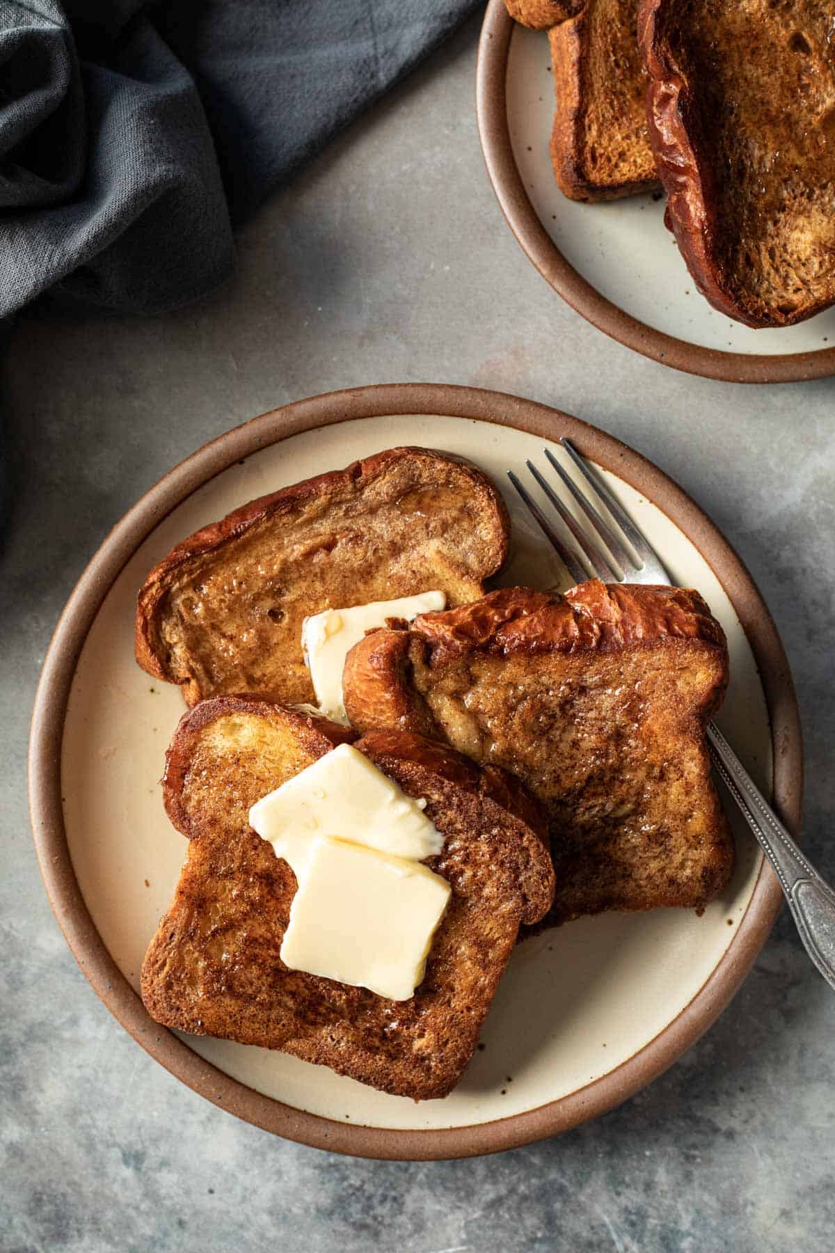 golden slices of French toast topped with butter and maple syrup stacked on a plate.