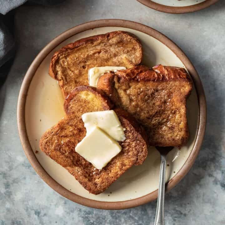 three slices of golden vegan French toast topped with two pats of butter plus maple syrup.