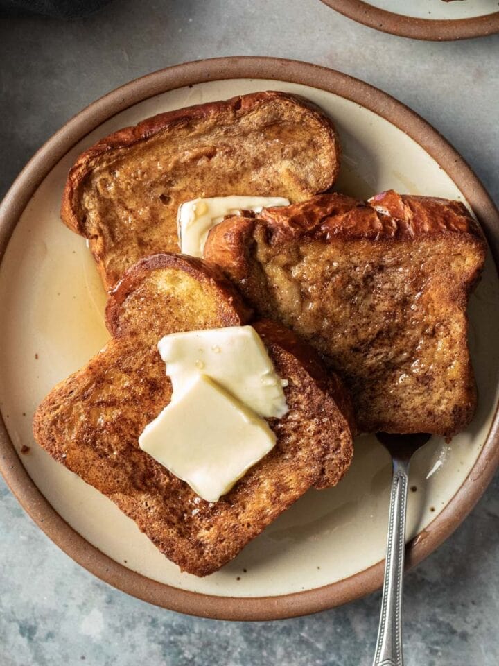 three slices of golden vegan French toast topped with two pats of butter plus maple syrup.