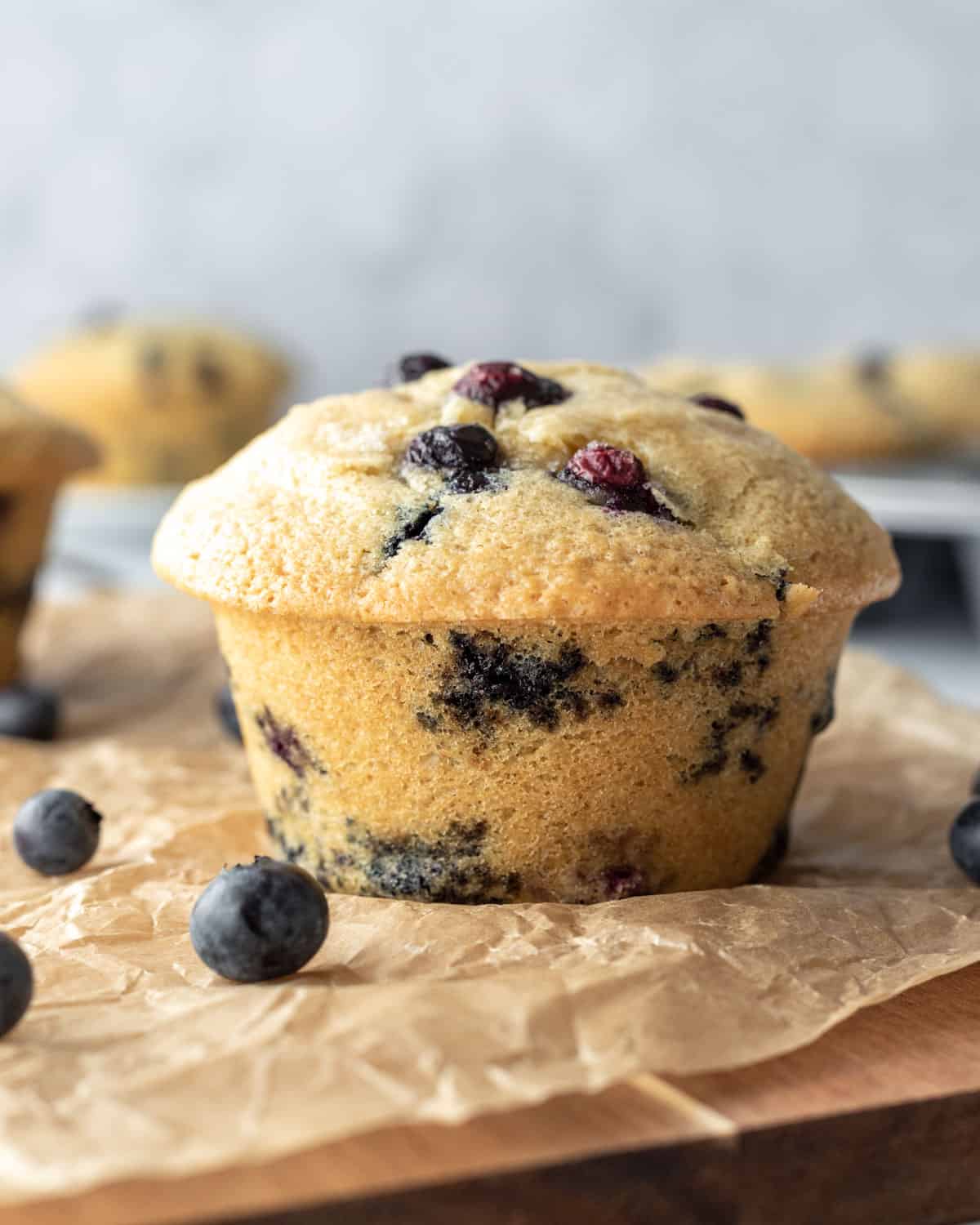 a large vegan blueberry muffin on parchment paper with fresh blueberries nearby.