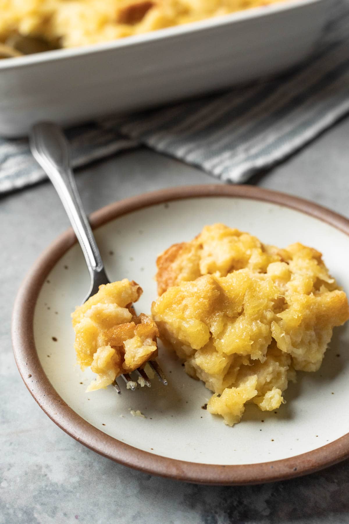 a serving of golden and buttery pineapple stuffing on a small plate with a bite on a fork.