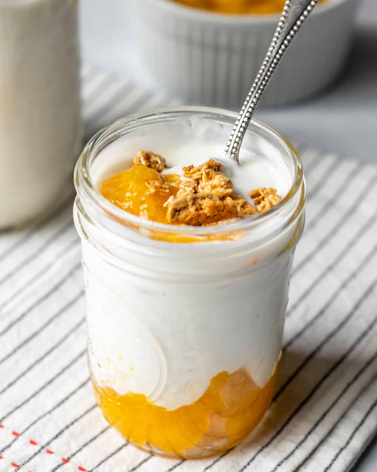 homemade vegan cashew yogurt layered with peach jam and granola in a glass jar.