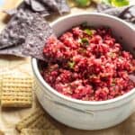 bright red cranberry salsa in a bowl surrounded by crackers and chips.