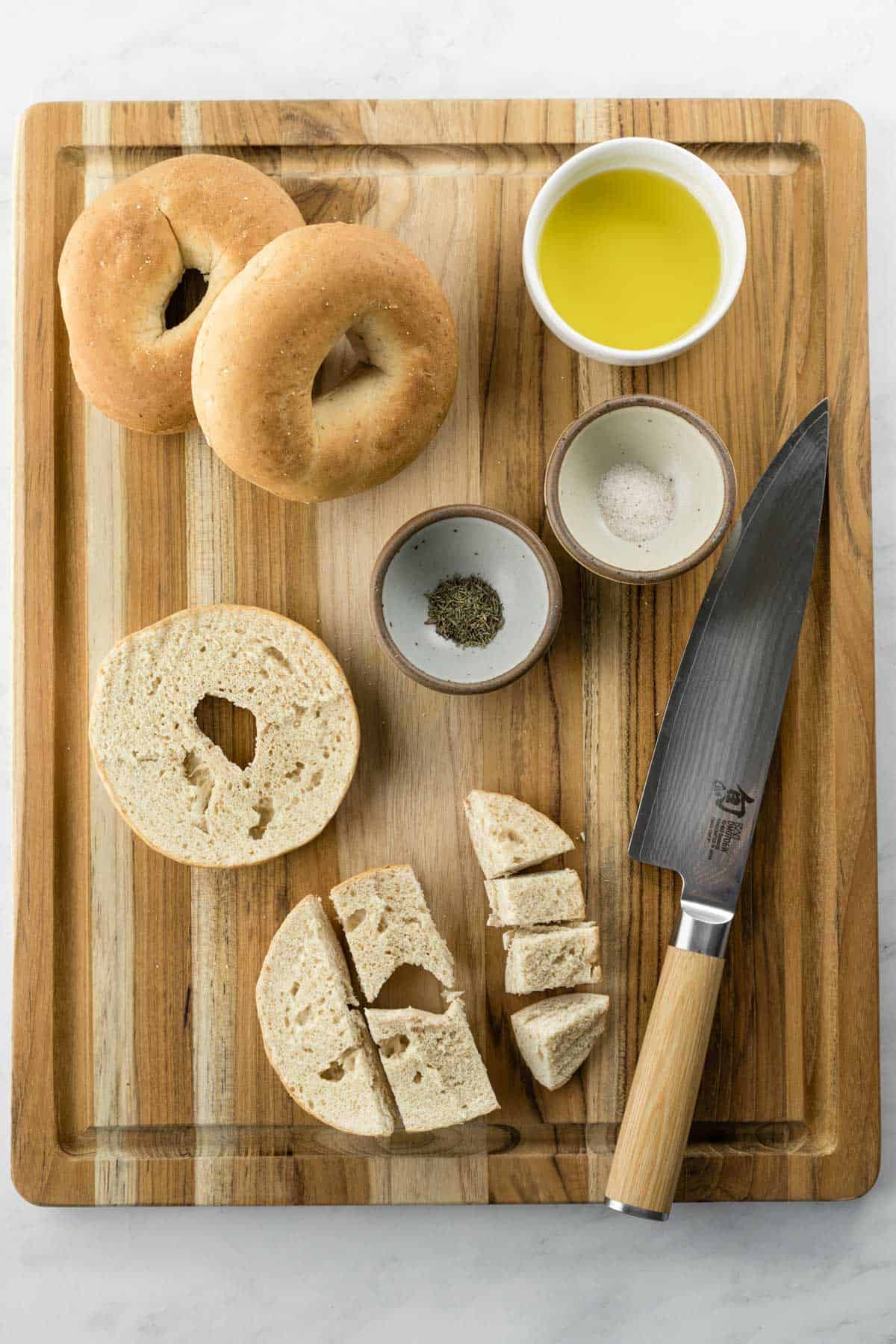 the ingredients needed to make croutons on a cutting board with a knife next to a cut bagel.
