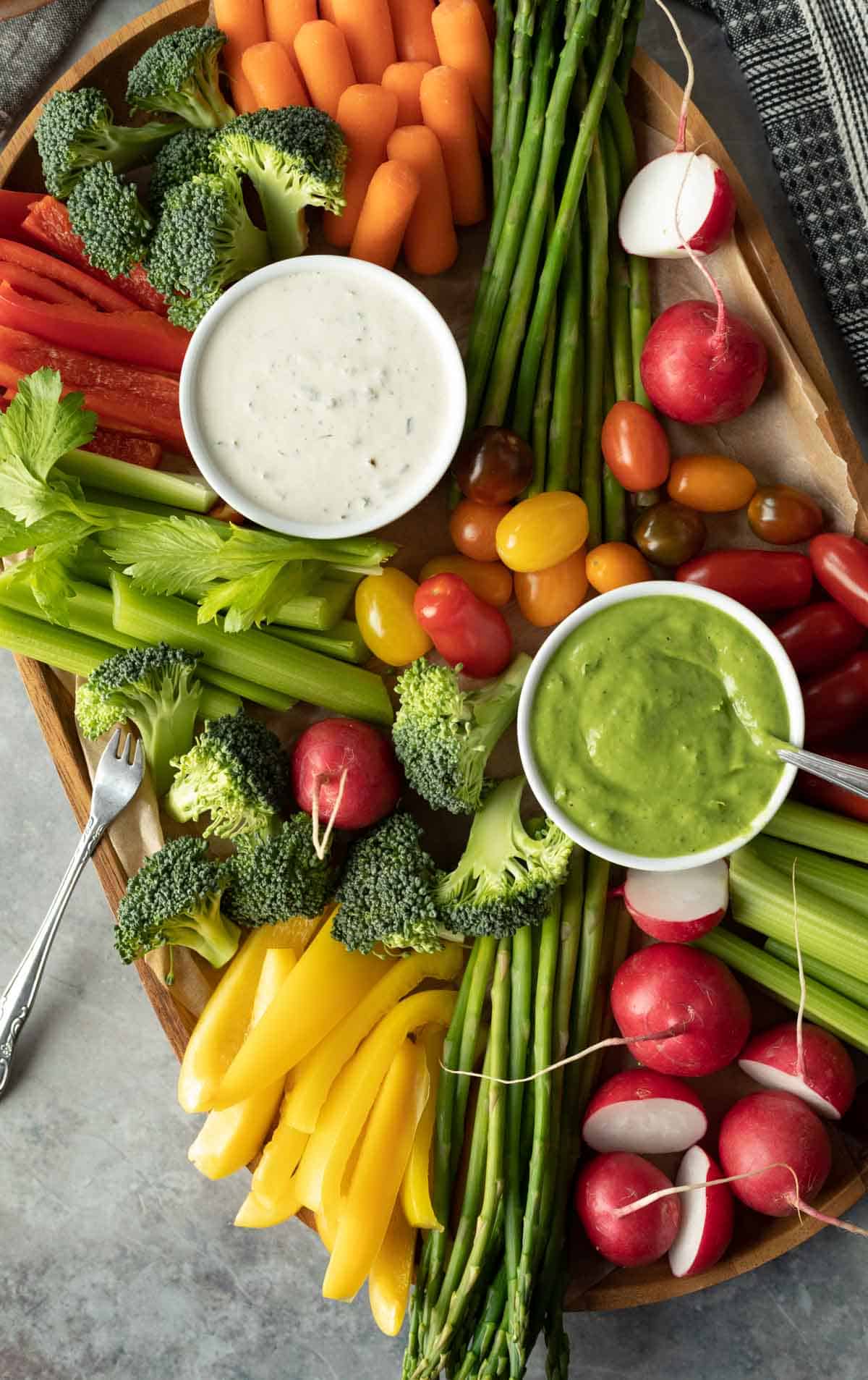 a veggie tray with a variety of red, orange, yellow, and green vegetables plus two homemade dips.